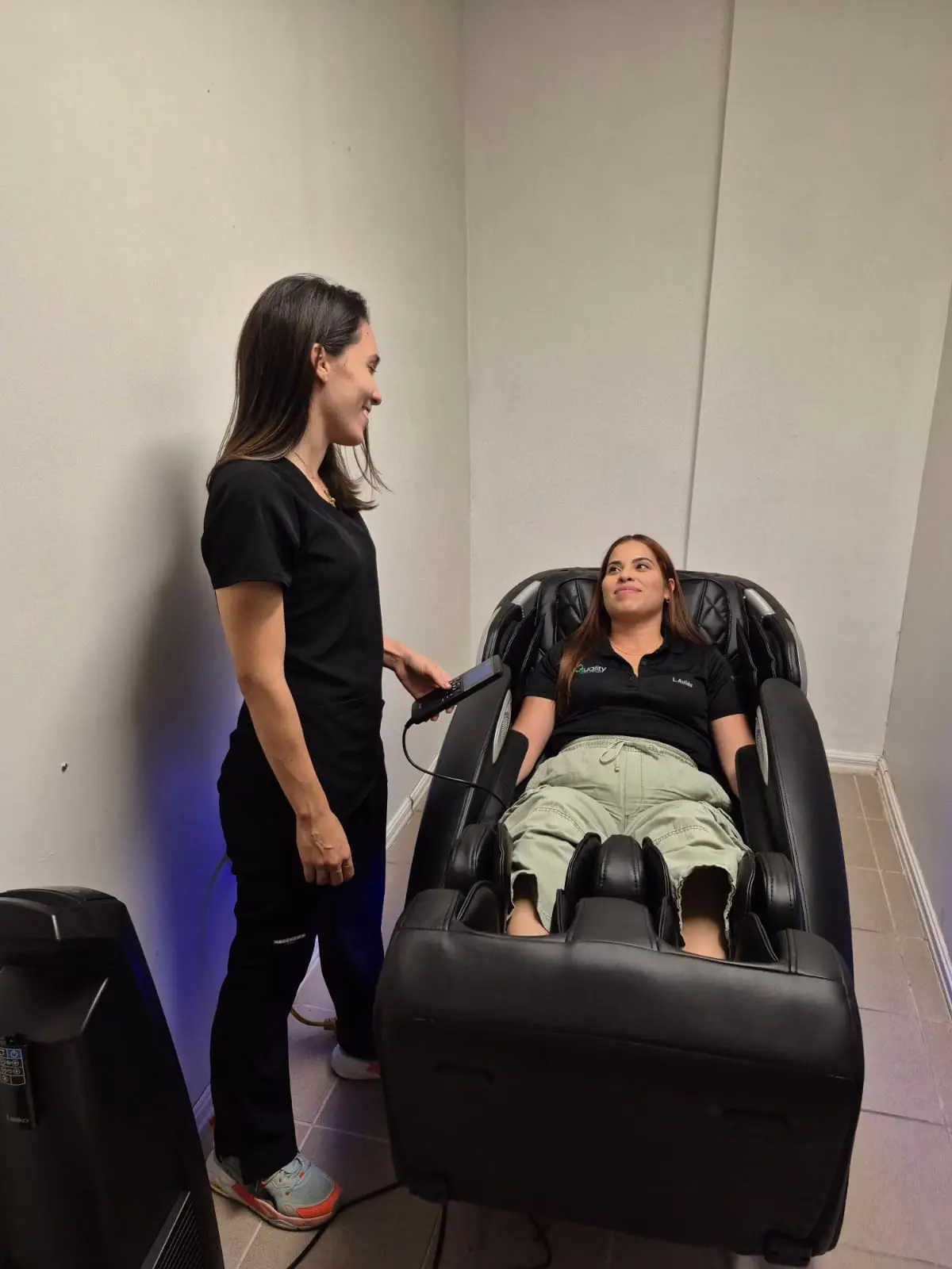 Doctora Jessica Rodriguez dando terapia de percusión rítmica con pistola terapéutica a hombre joven que esta sentado.